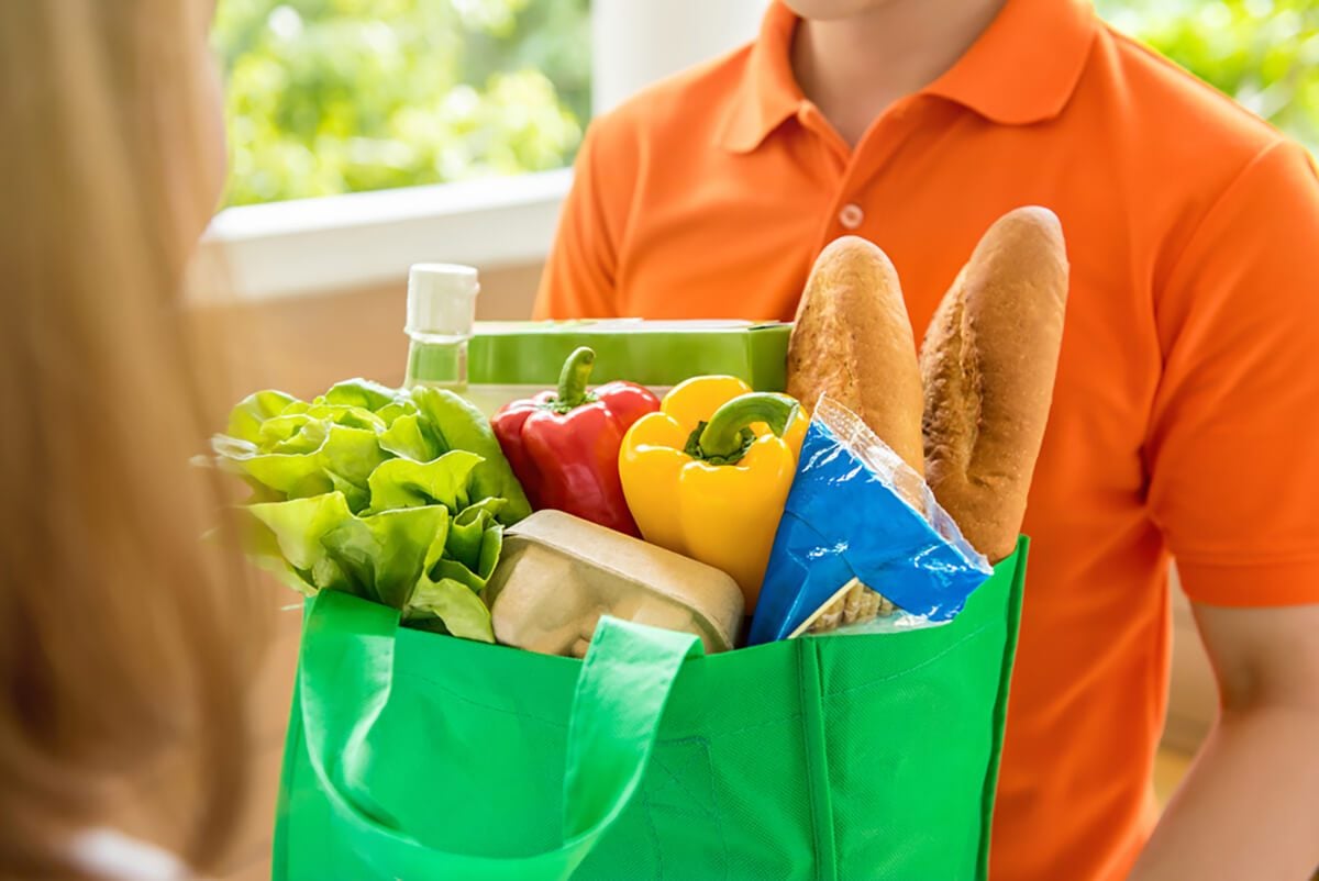 一名穿着橙色polo衫的杂货店送货员正在给一名在家的妇女送餐