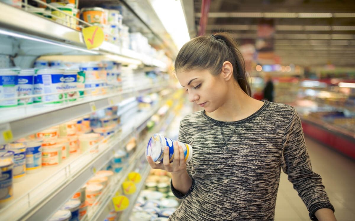 年轻女子在购买前阅读乳制品的成分、声明或有效期。好奇的女人阅读食物的营养价值。在超市杂货店购物