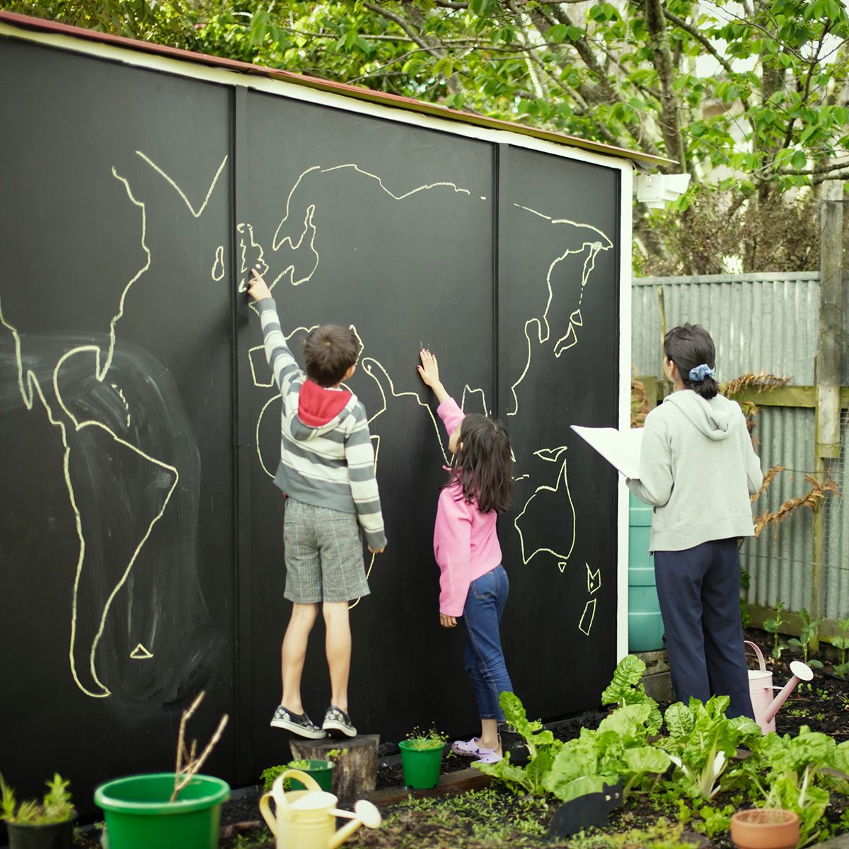 母亲和孩子在花园黑板上比较地图集图片和世界地图。
