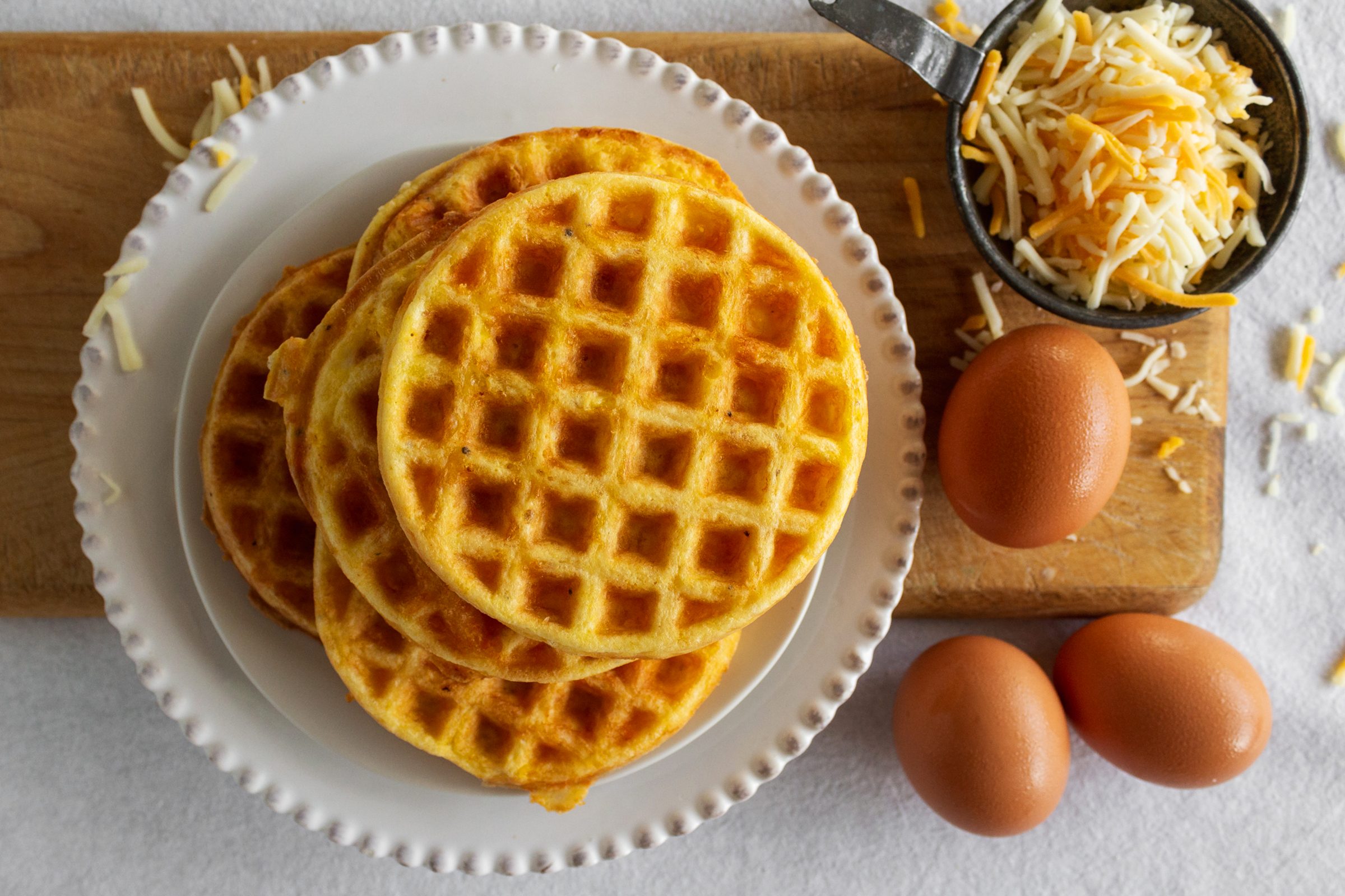 烤好的Chaffles放在盘子上，鸡蛋和奶酪放在木板上
