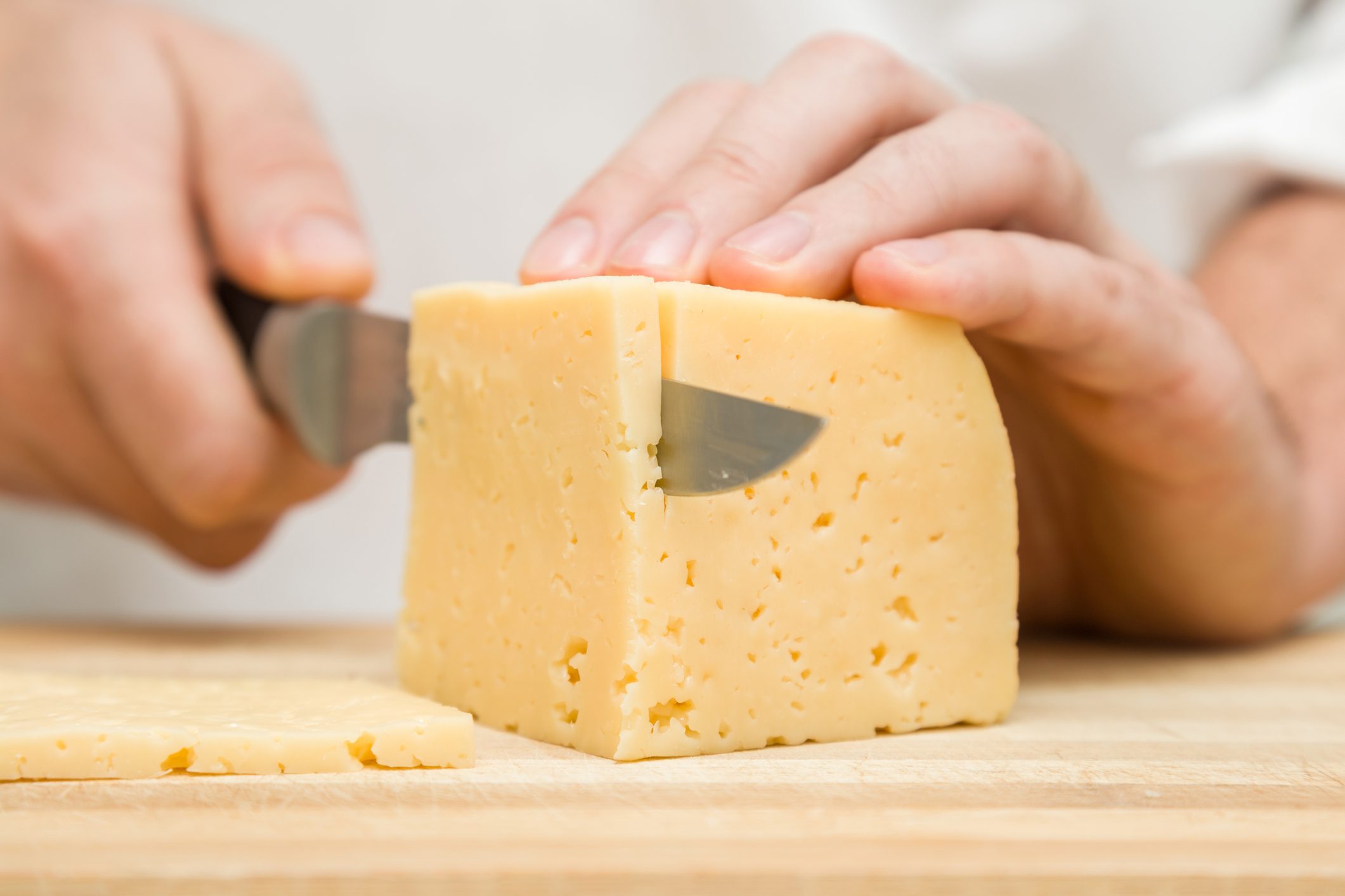 厨师的手用刀切割木板上的奶酪