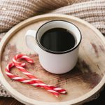 白色的咖啡放在木桌上，米色的针织面料和红色的拐杖糖。圣诞节舒适的静物生活。
